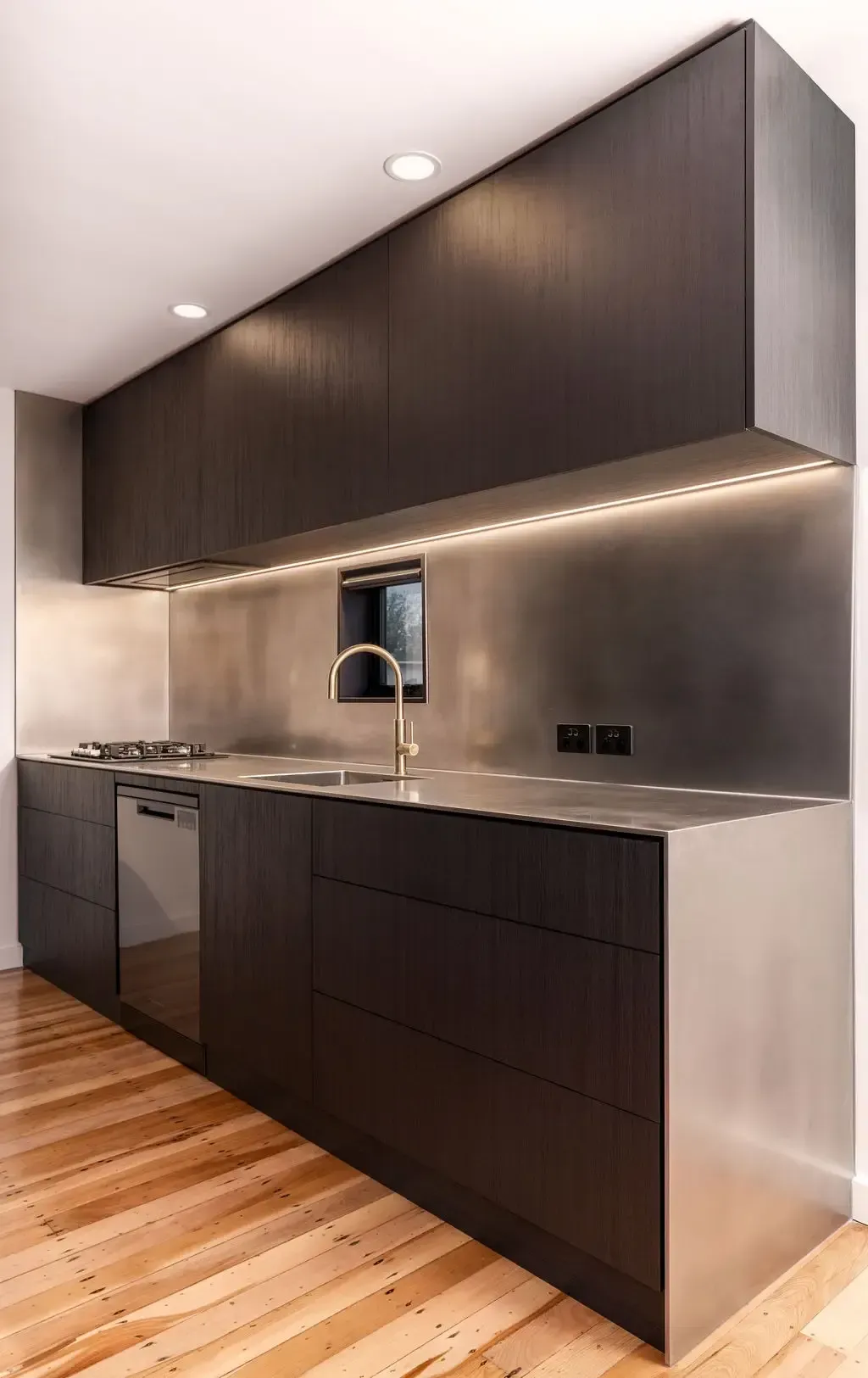 Modern kitchen with dark wood cabinets, stainless steel countertop, and gold faucet.