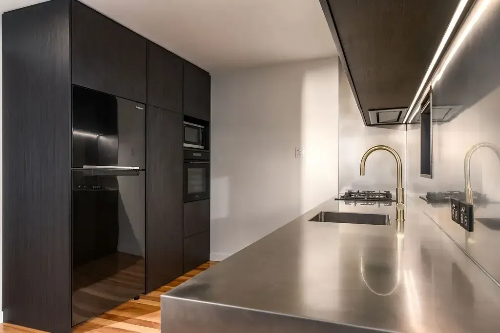 Modern kitchen with dark cabinets, stainless steel countertop and gold faucet.