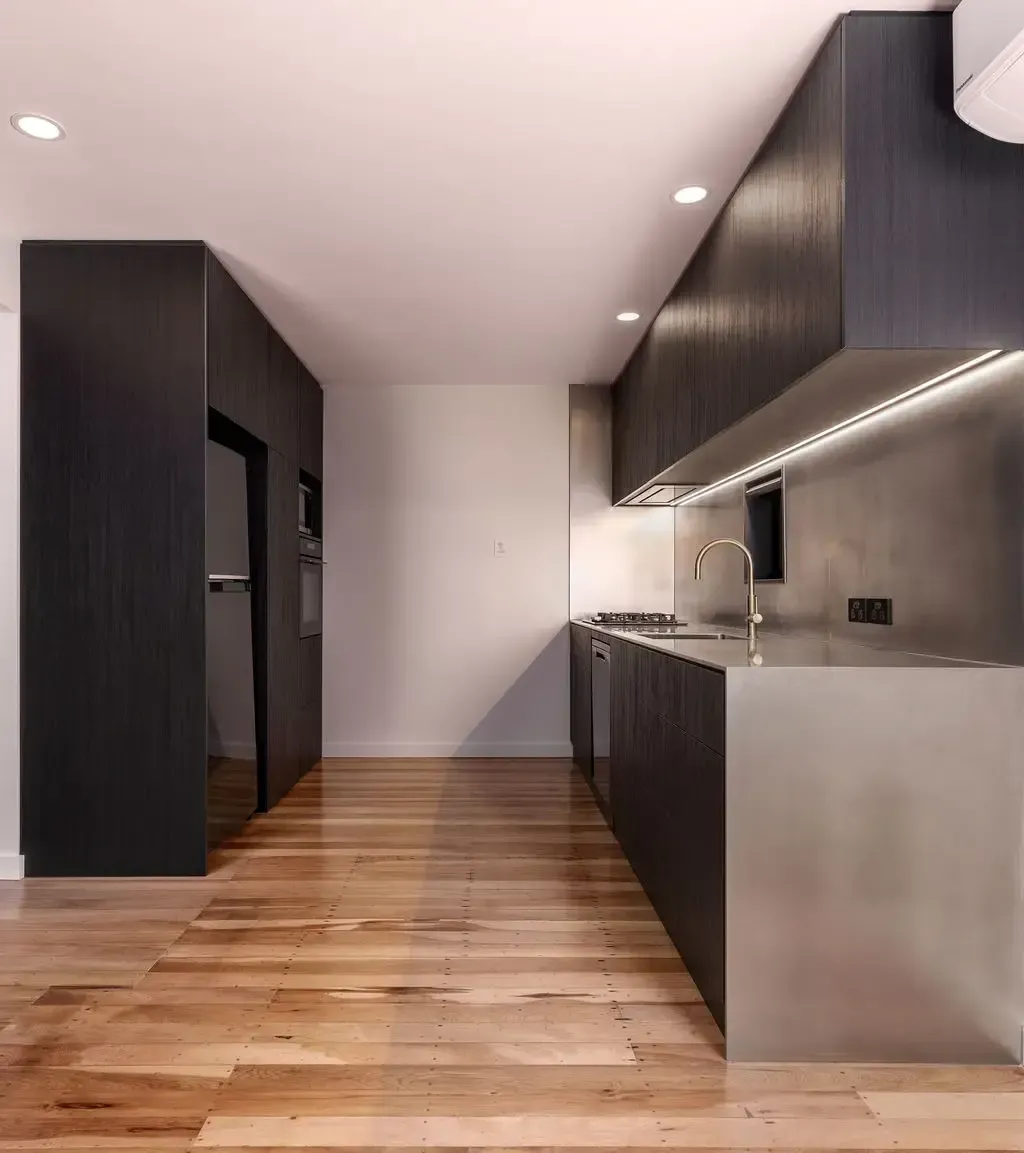Modern kitchen with dark wood cabinets, stainless steel counter, and wooden floor.