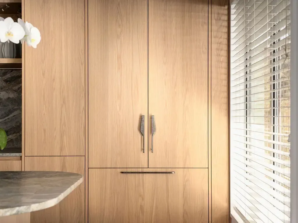 Light wood built-in refrigerator with silver handles, part of a kitchen design with window.