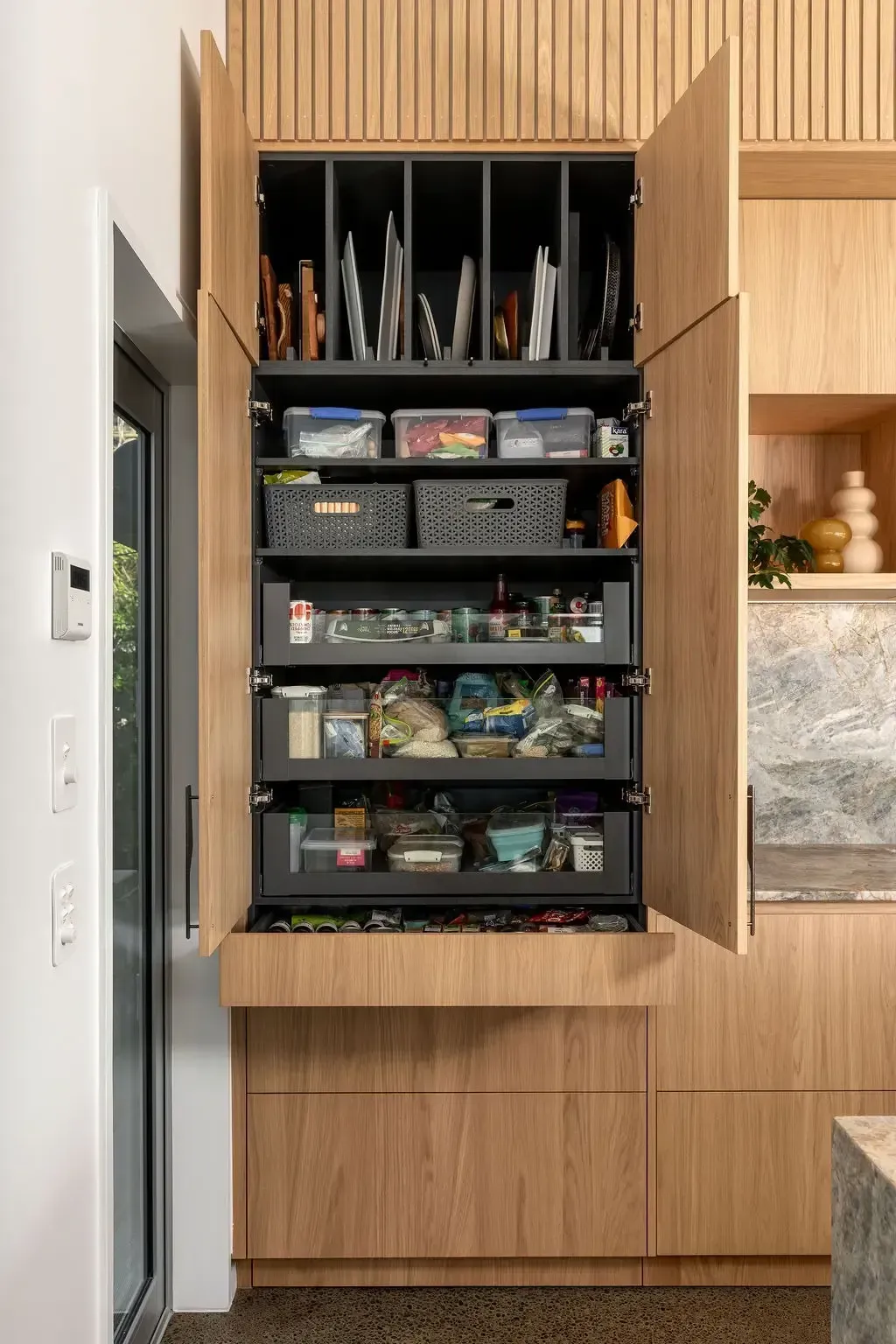 A modern kitchen pantry with pull-out shelves and vertical dividers for baking sheets, and food storage.