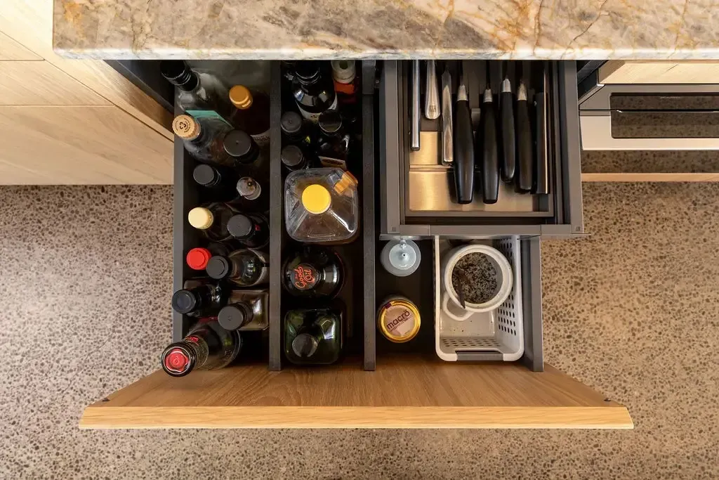 Open kitchen drawer with spices, knives, and a grater.