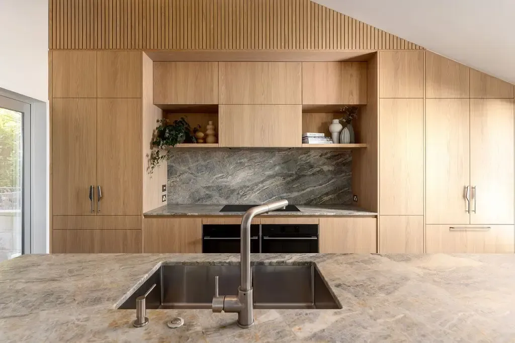 Wooden kitchen with a gray countertop and sink, cabinets, and marble backsplash.