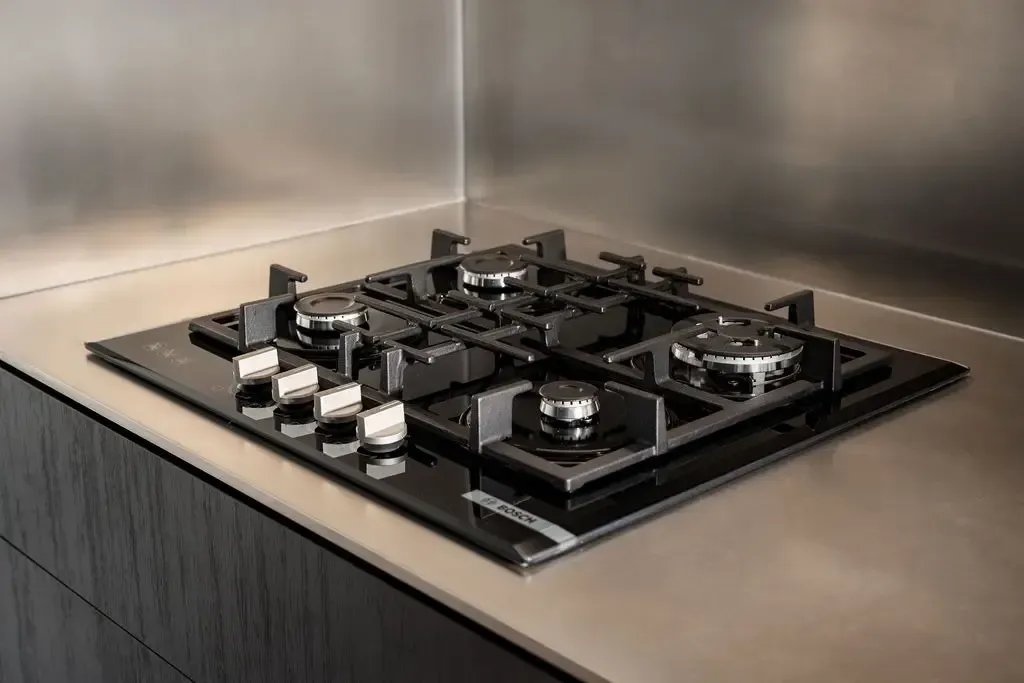 Black gas cooktop with four burners on a stainless steel countertop, in a modern kitchen.