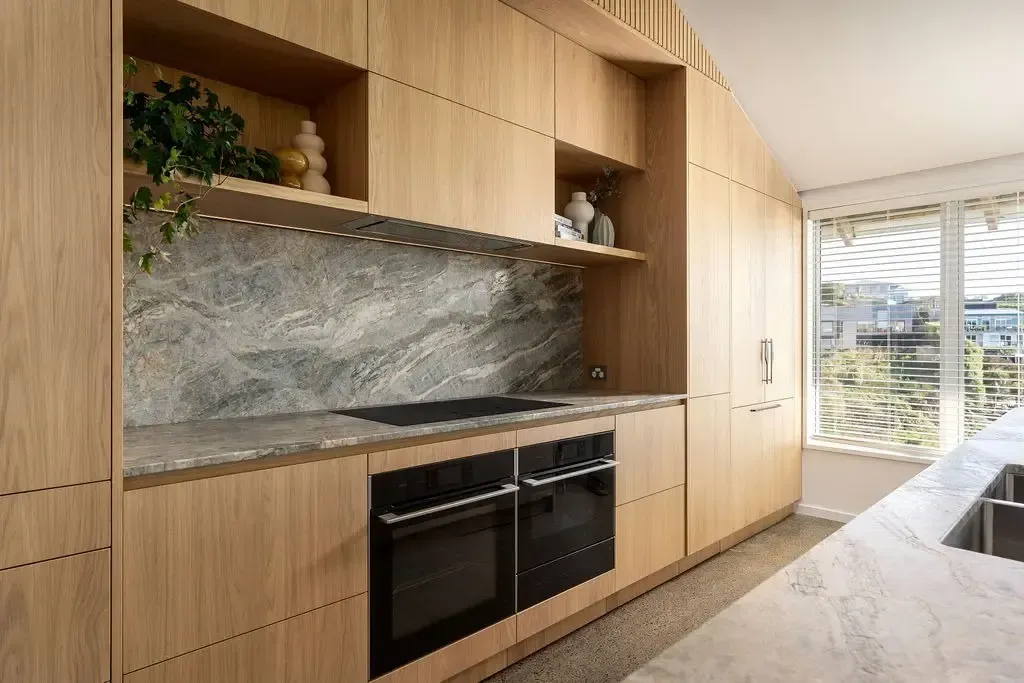 Light wood kitchen with integrated appliances, gray countertop and backsplash, and a window.