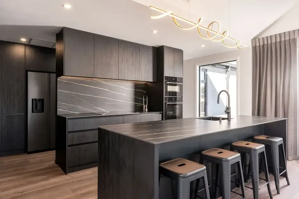 Modern black kitchen with island, stools, and appliances; neutral tones, wood floors.