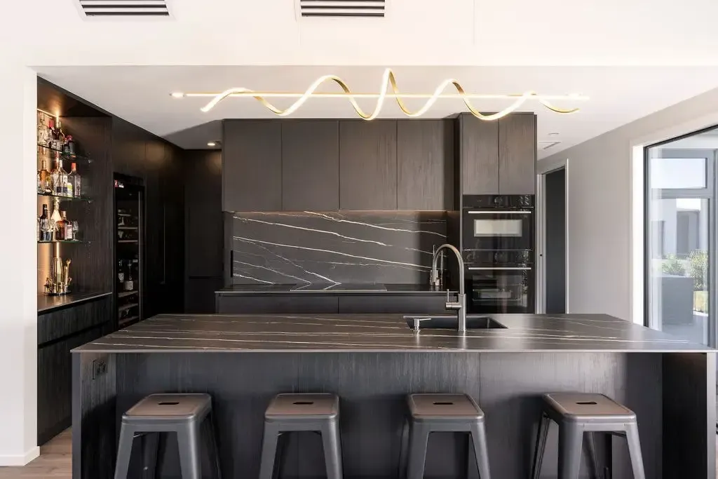 Modern black kitchen with island, stools, and gold accent lighting.