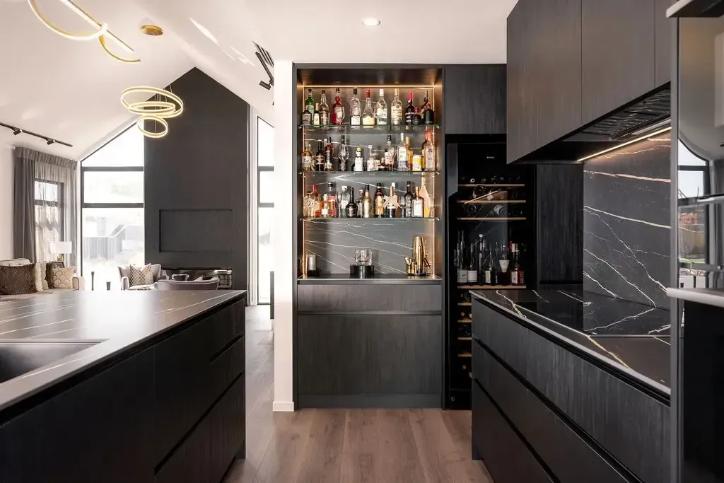 Modern black kitchen with bar, wine fridge, and light fixtures.