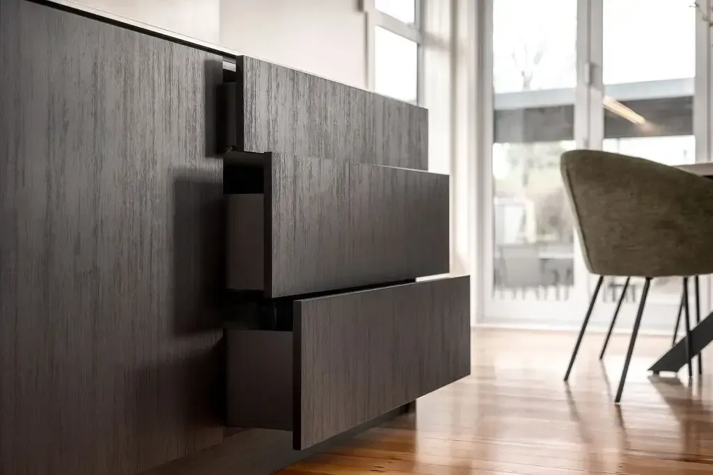 Dark wood drawers partially open in a modern interior. A chair and window are in the background.