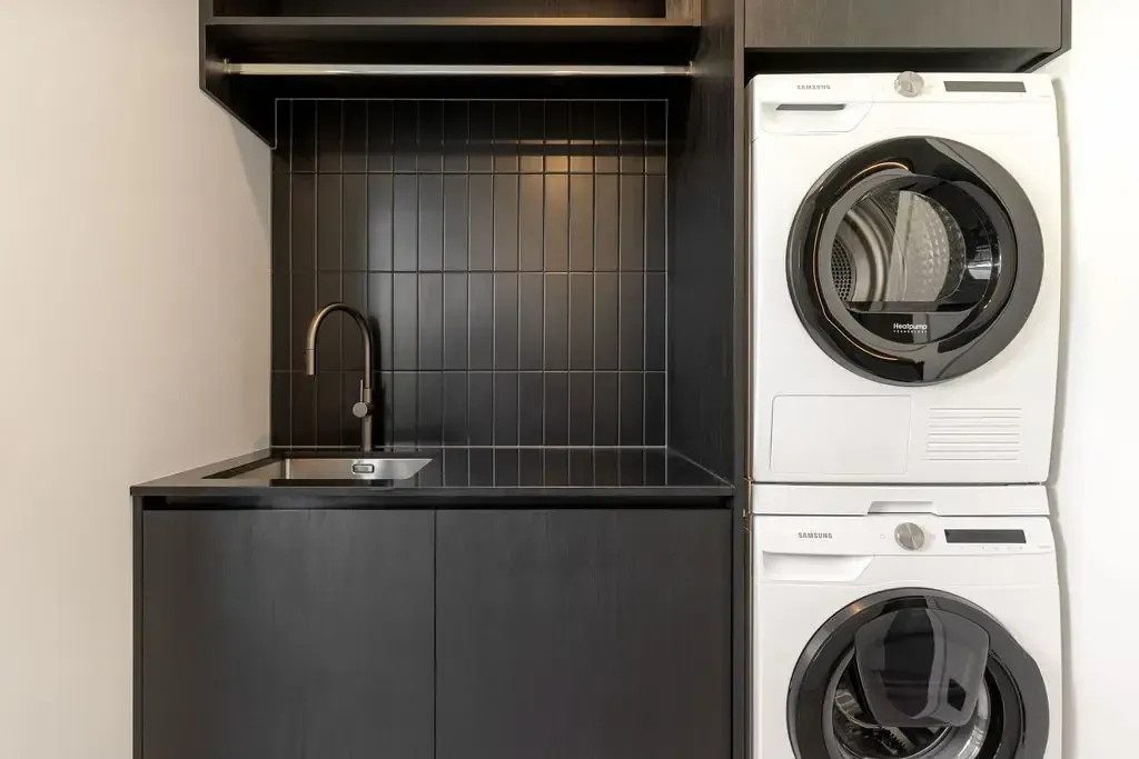 Laundry room with black cabinets and backsplash. Stacked white washer and dryer.