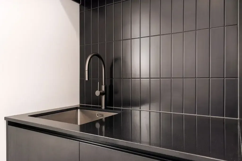 Black tiled backsplash and countertop with silver sink and faucet.