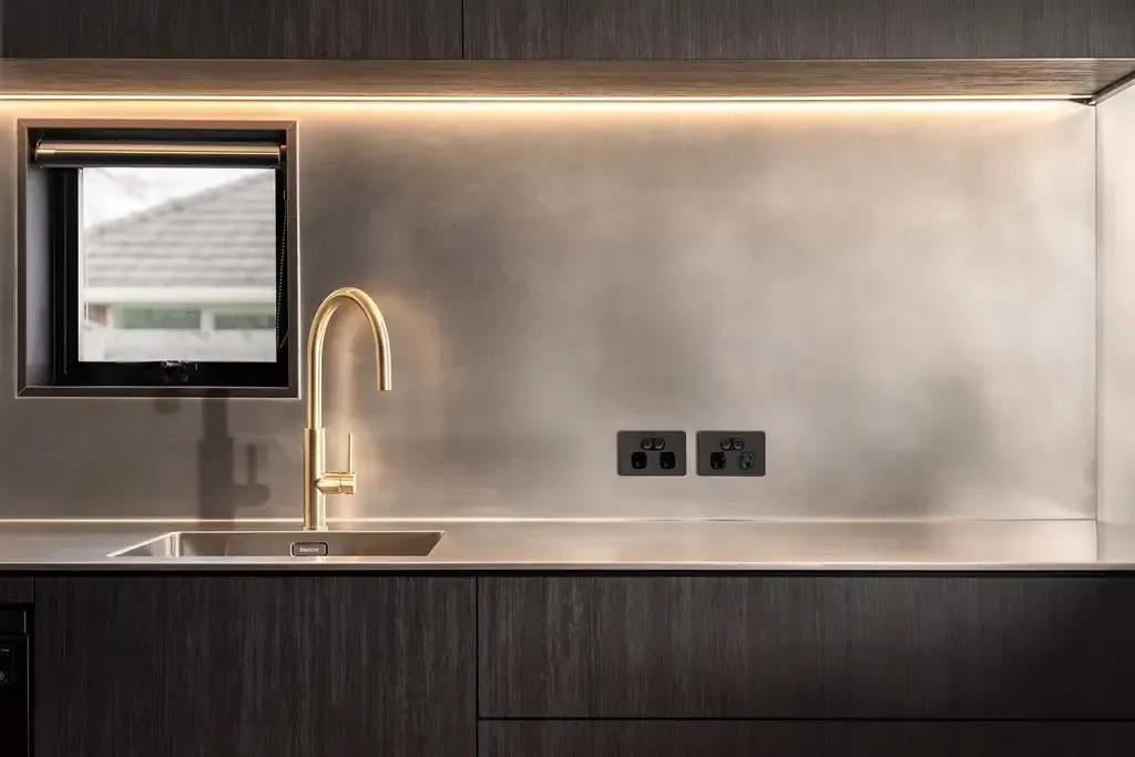 Modern kitchen with gold faucet, stainless steel backsplash, and window. Dark wood cabinetry and countertop.