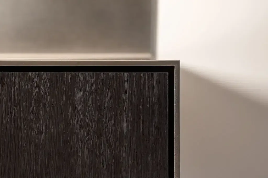 Close-up of a dark wood cabinet corner against a white wall with a shadow.