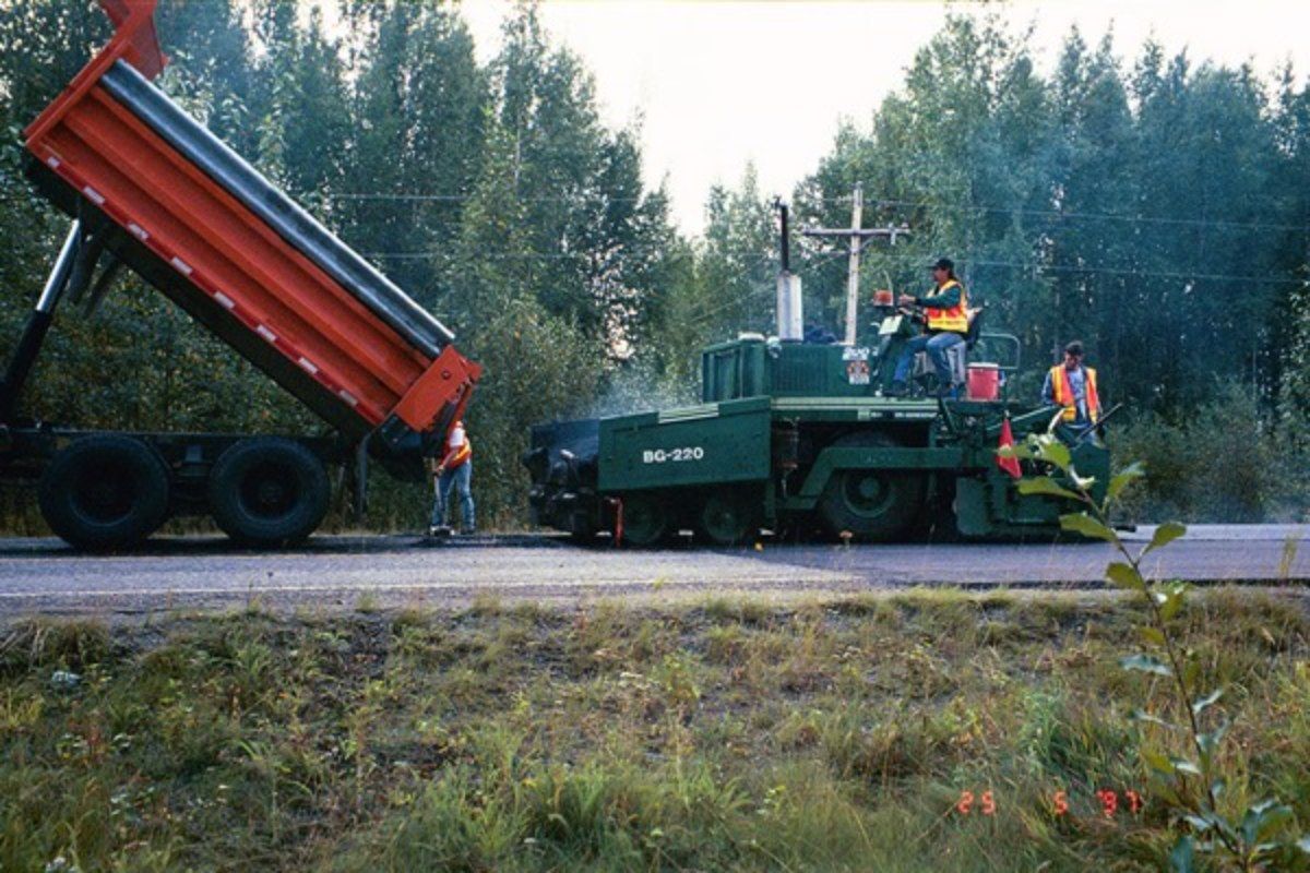 A truck is being loaded with paving on a road.