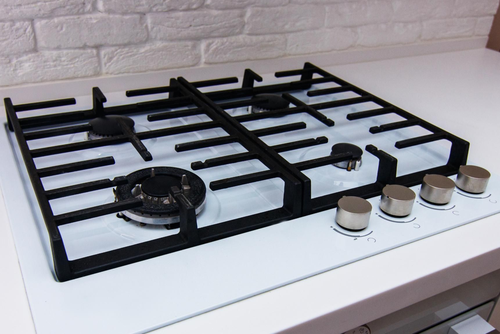 White gas stovetop with black grates and four control knobs against a tiled backsplash