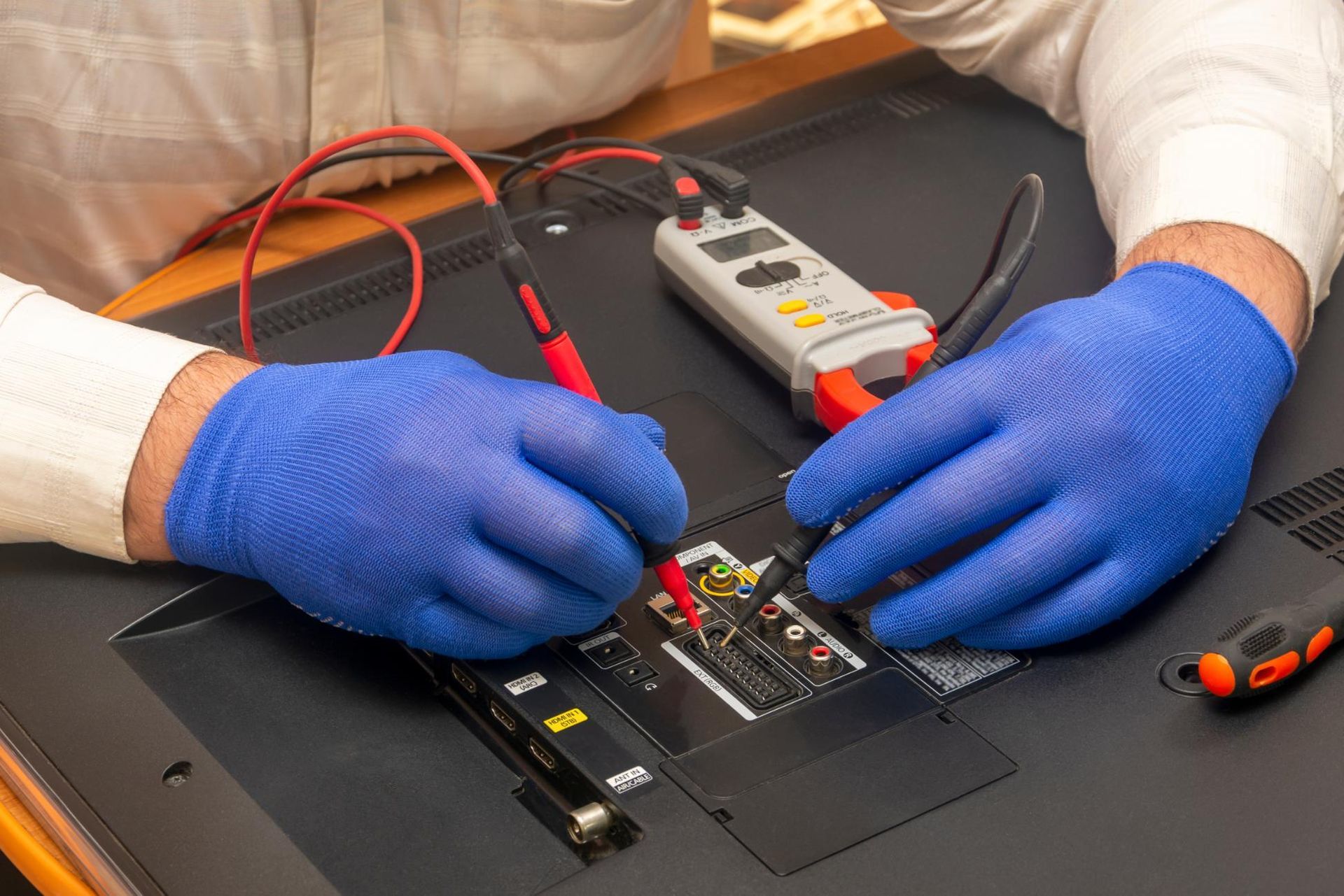 Gloved hands using probes to test an electronic circuit board on a workbench