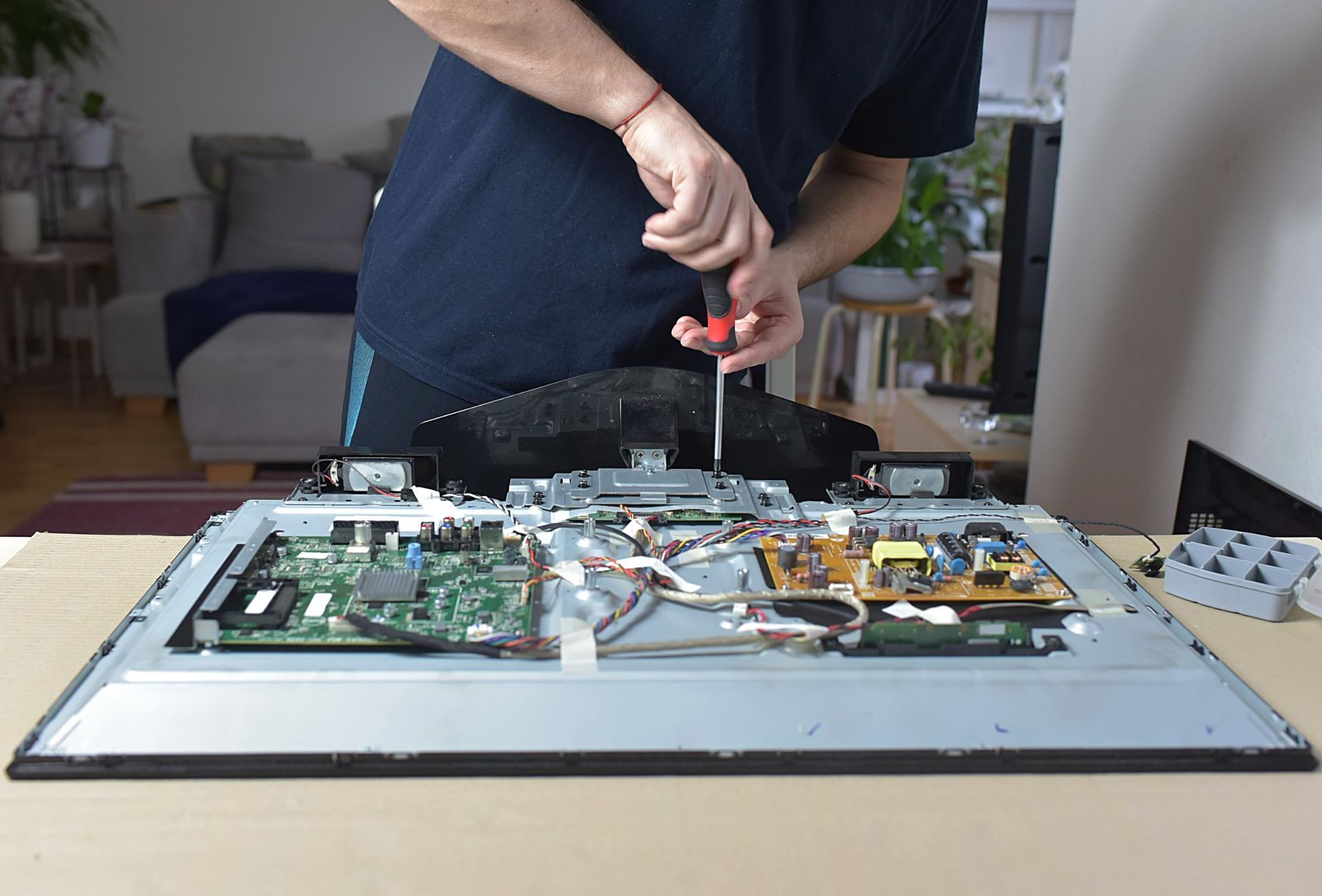 Person using a screwdriver to repair the opened back of a flat-screen TV on a table
