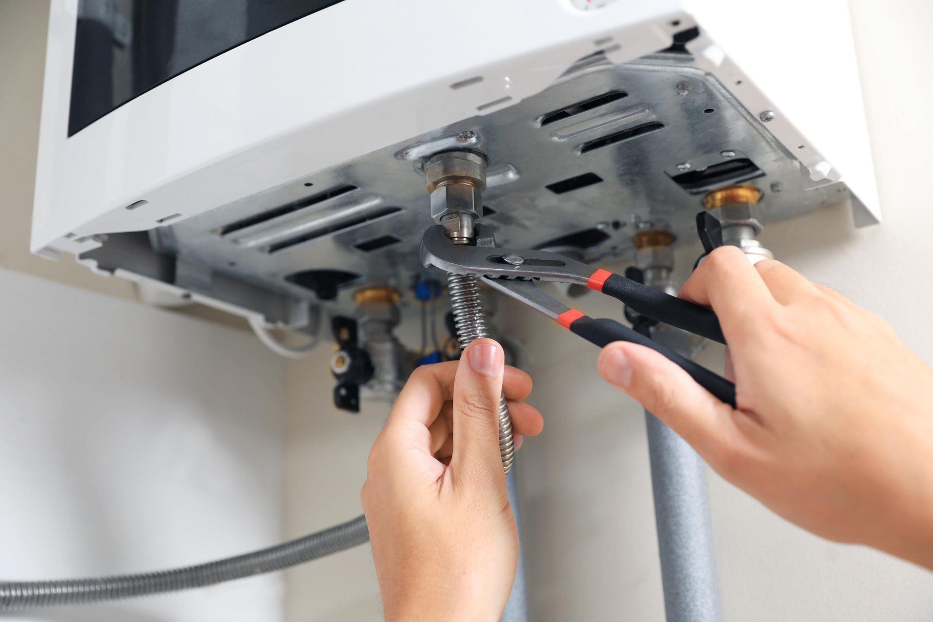 Hands tightening a wall-mounted appliance under a cabinet with a wrench and pliers