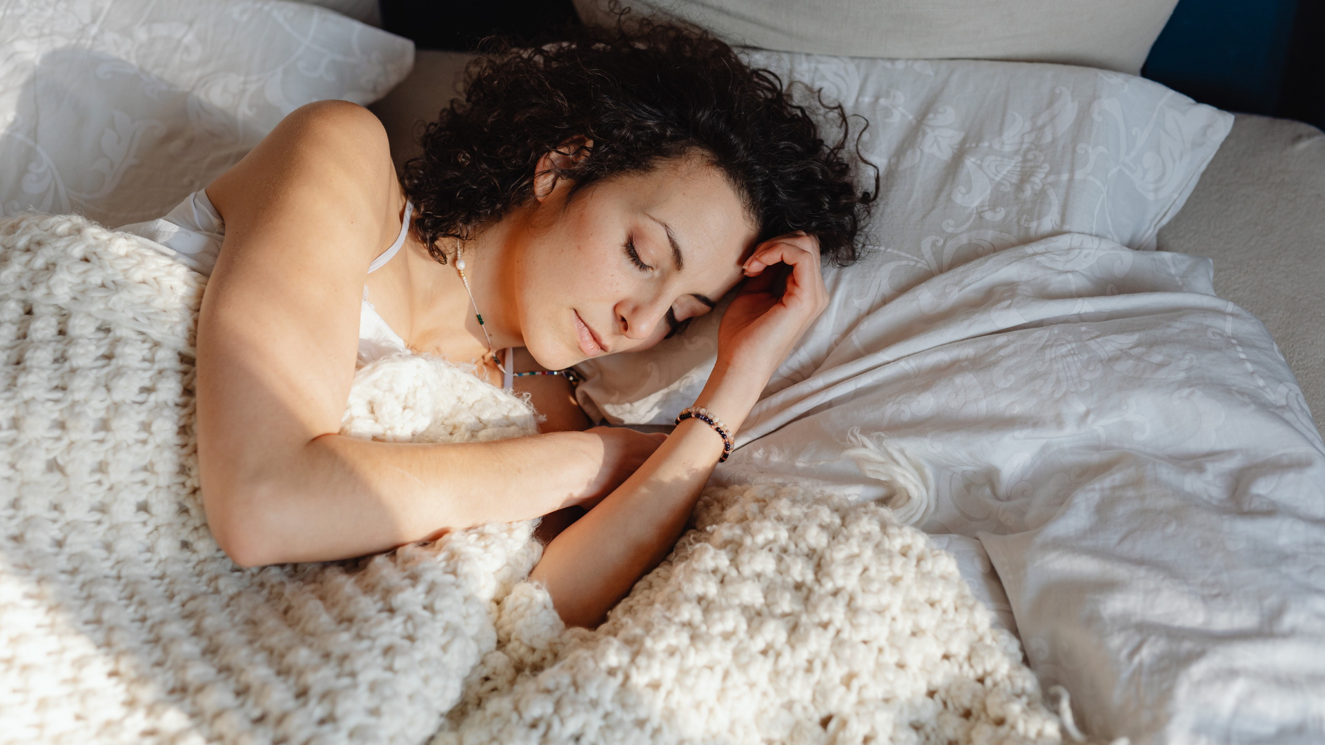 Woman sleeping peacefully in bed, covered with a thick white blanket, sunlight on her face.