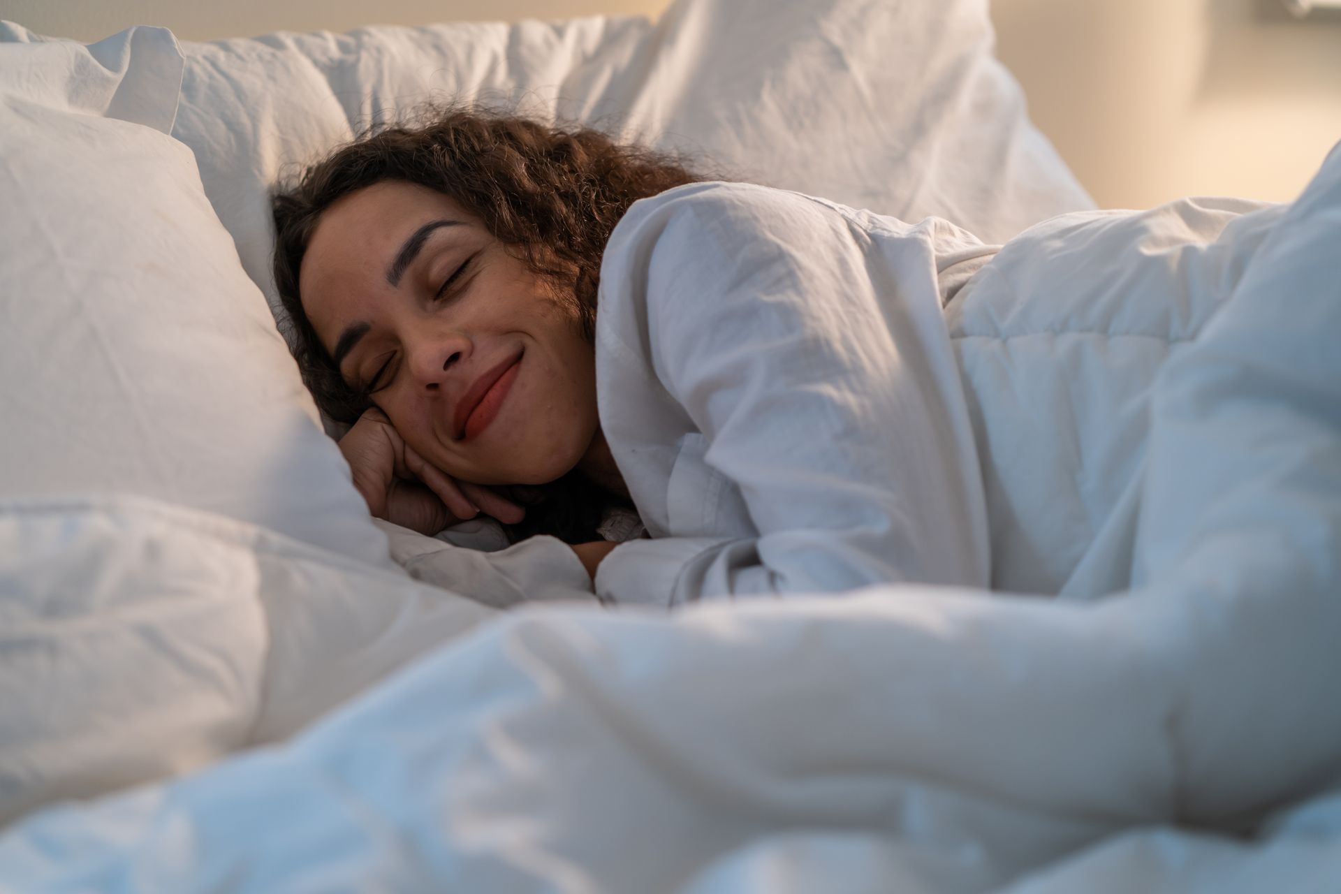 A woman is sleeping in a bed with white sheets and pillows.