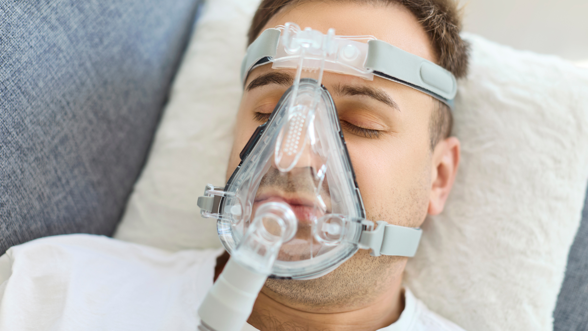 Man wearing a CPAP mask, lying down on a pillow.
