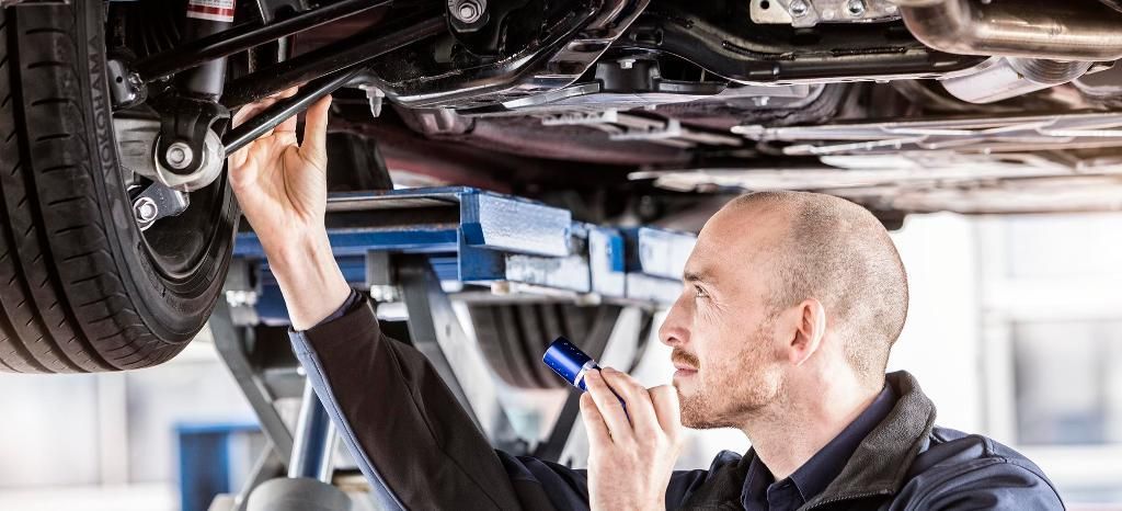 A man is working on the underside of a car in a garage. | TIRE NATION & AUTO REPAIR POINT S