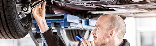 A man is working on the underside of a car in a garage. | TIRE NATION & AUTO REPAIR POINT S