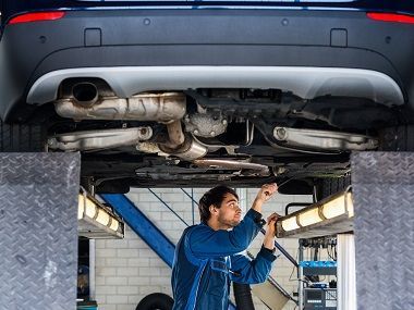 A man is working on the underside of a car in a garage. | TIRE NATION & AUTO REPAIR POINT S