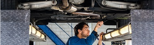 A man is working on the underside of a car in a garage. | TIRE NATION & AUTO REPAIR POINT S