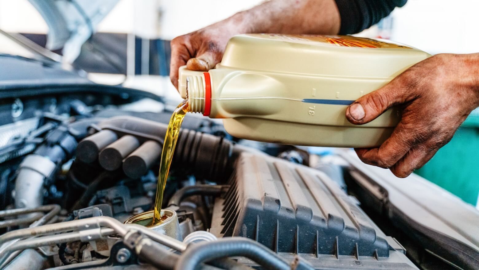 A man is pouring oil into a car engine. | TIRE NATION & AUTO REPAIR POINT S