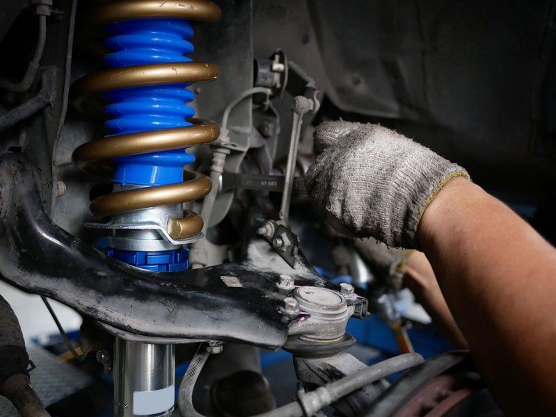 A person is working on a shock absorber on a car with a wrench. | TIRE NATION & AUTO REPAIR POINT S
