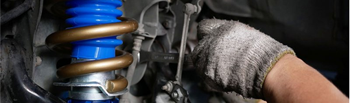 A person is working on a shock absorber on a car with a wrench. | TIRE NATION & AUTO REPAIR POINT S