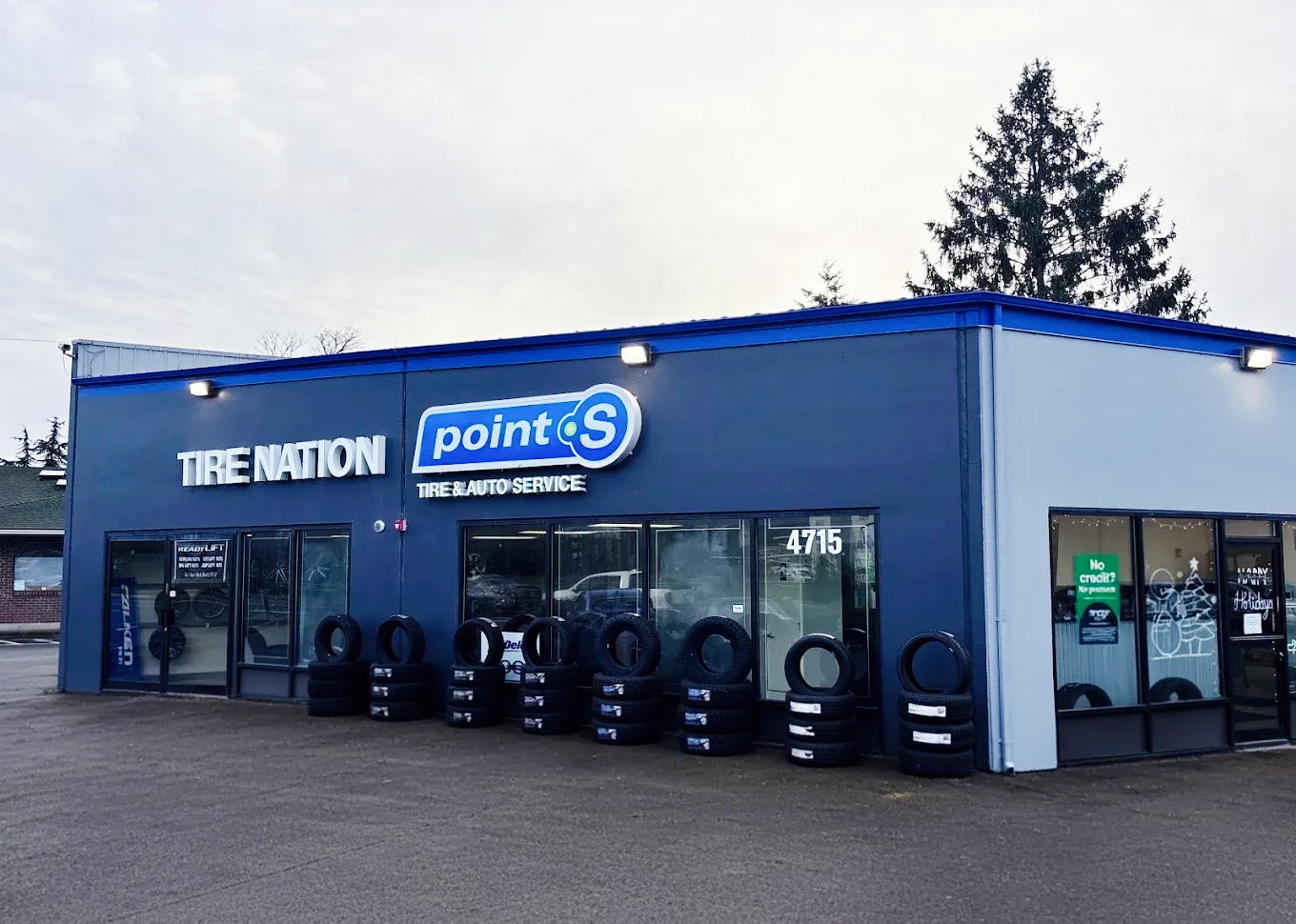 A row of tires are stacked in front of a tire shop. | TIRE NATION & AUTO REPAIR POINT S