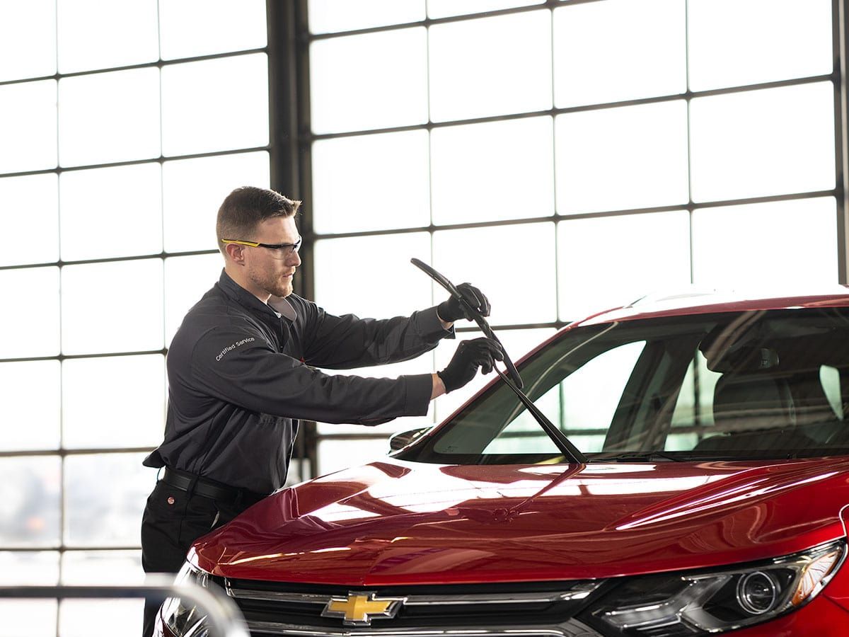A man is cleaning the windshield of a red car in a garage. | TIRE NATION & AUTO REPAIR POINT S