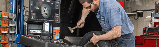 A man is working on a tire with a hammer in a garage. | TIRE NATION & AUTO REPAIR POINT S