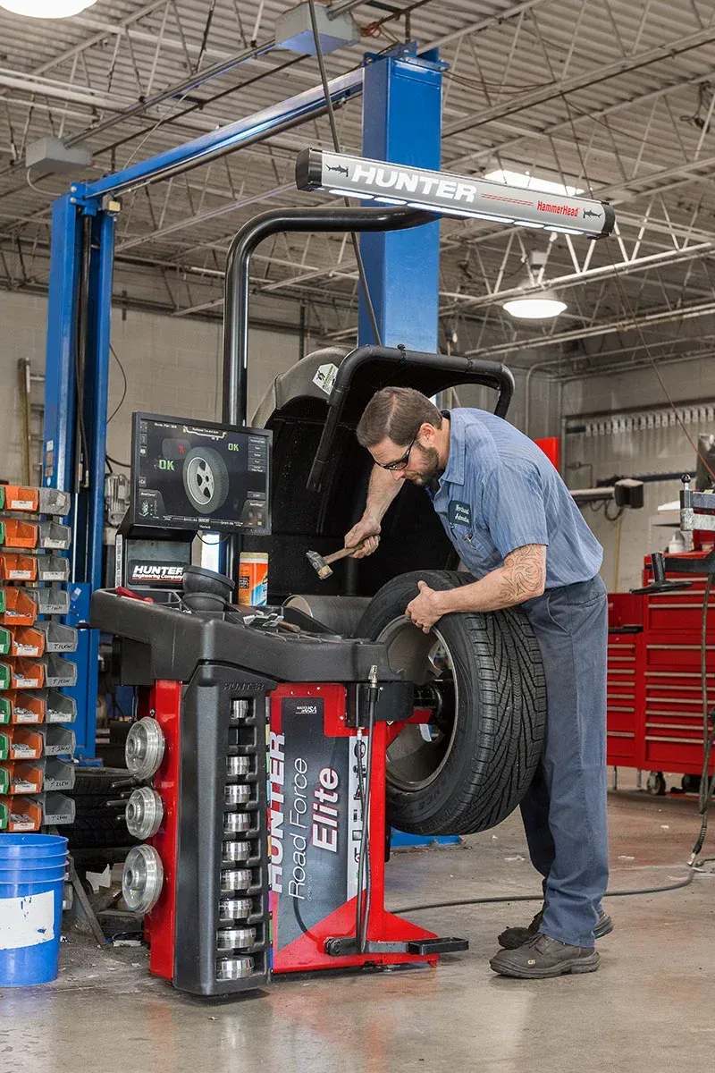 A man is balancing a tire on a machine in a garage. | TIRE NATION & AUTO REPAIR POINT S