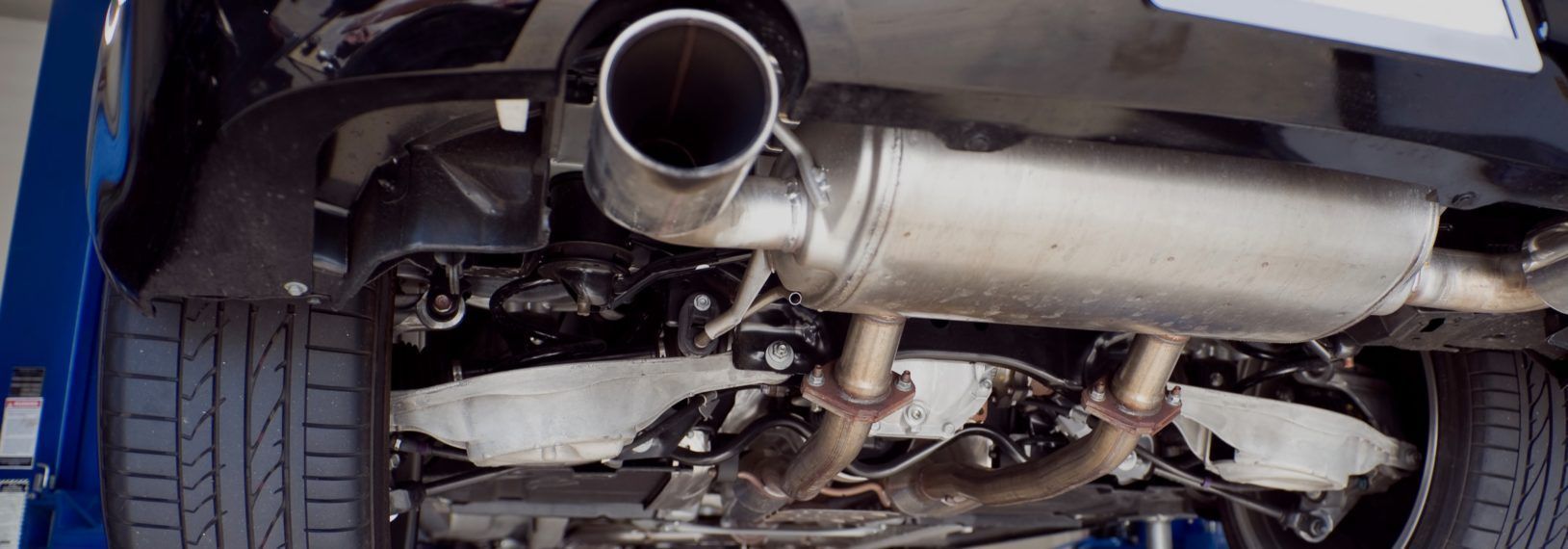 A close up of a car exhaust pipe on a lift. | TIRE NATION & AUTO REPAIR POINT S
