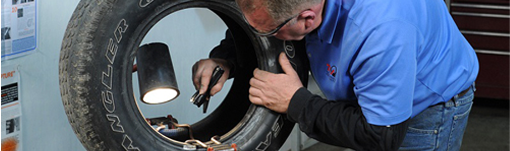 A man in a blue shirt is working on a tire. | TIRE NATION & AUTO REPAIR POINT S