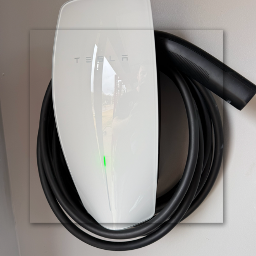 White EV charging, plugged into a white car against a gray wall, a charger displays 90%.