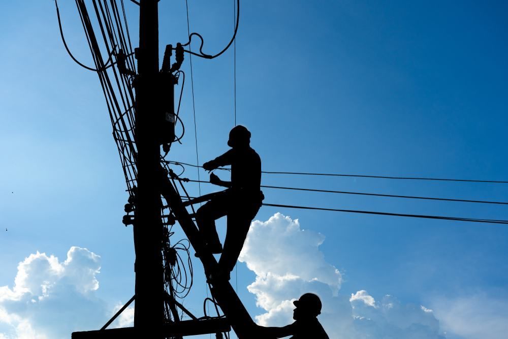 Two Men Are Working On A Power Pole With A Blue Sky In The Background — Accent Electrics In Noraville, NSW