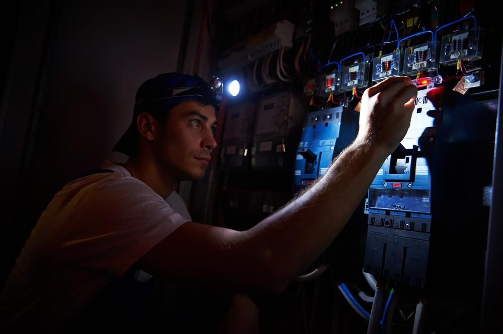 A Man Is Working On An Electrical Panel In The Dark With A Flashlight — Accent Electrics In Wyong, NSW