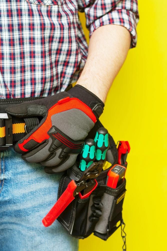 A Man Wearing Gloves And A Tool Belt Is Holding A Pair Of Pliers — Accent Electrics In Bateau Bay, NSW