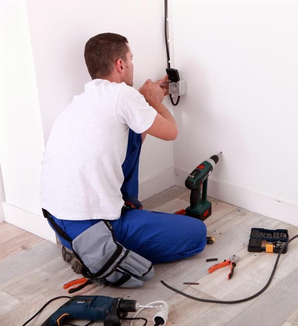 A Man Is Sitting On The Floor Working On A Wall — Accent Electrics In Noraville, NSW