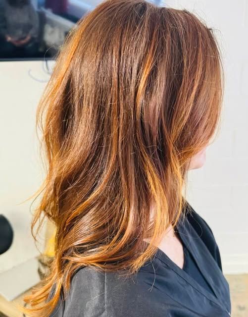 Woman with wavy auburn hair with highlights. She's wearing a black shirt, indoors.