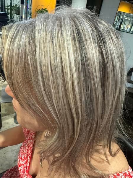 Woman with layered, ash blonde and silver hair, wearing a floral top.