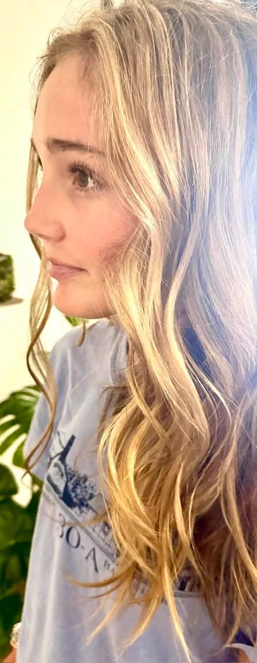 A woman with blonde hair and a light blue shirt. She is looking to the side.