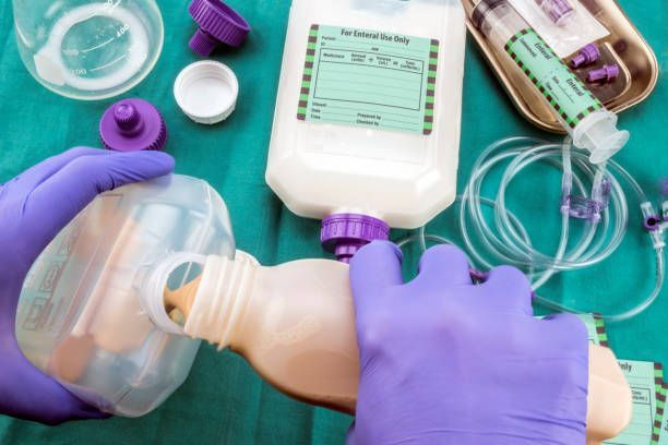 Hands in purple gloves pouring fluid from a bottle into a container, preparing intravenous medication.