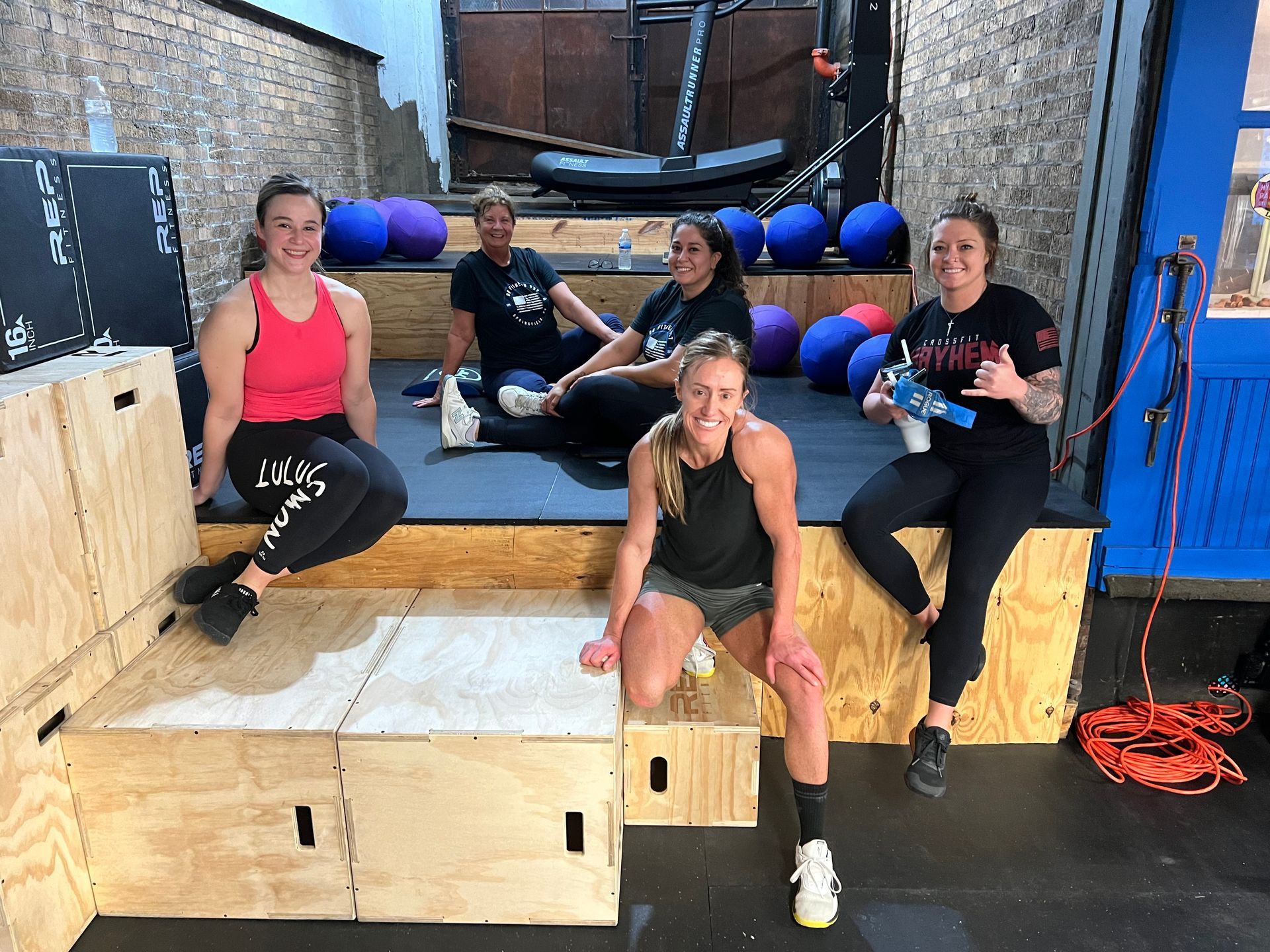 A group of women are sitting on wooden boxes in a gym.