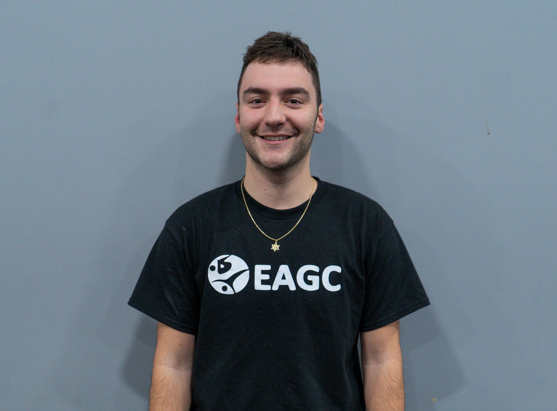 A man wearing a black eagc t-shirt is smiling for the camera.