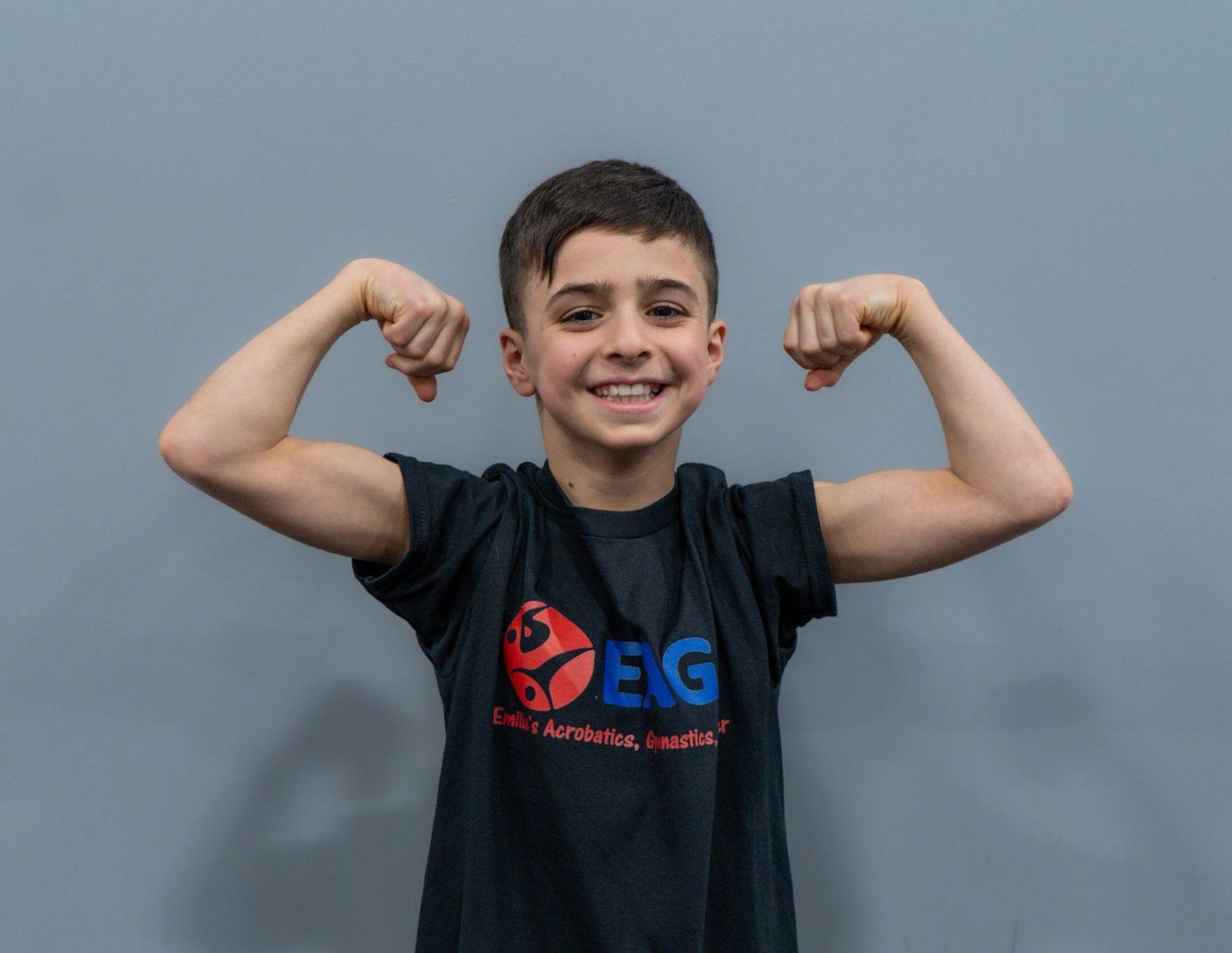A young boy in a black shirt is flexing his muscles.